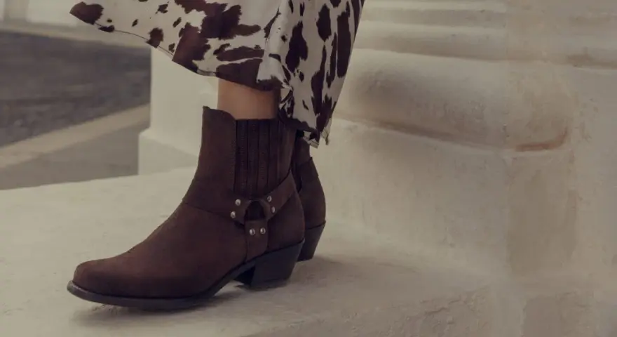 Brązowe kowbojki z klamrą i wzorzysta sukienka tworzą modne kowbojki stylizacje.