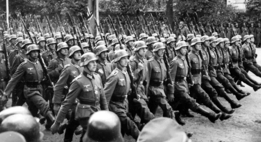 Żołnierze SS maszerują w zwartym szyku, niosąc karabiny. Ich charakterystyczne mundury, których projektant pozostaje nieznany, budzą grozę.