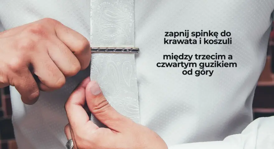 Mężczyzna zapina spinkę do krawata i koszuli między trzecim a czwartym guzikiem od góry. Elegancki sposób na noszenie krawata.