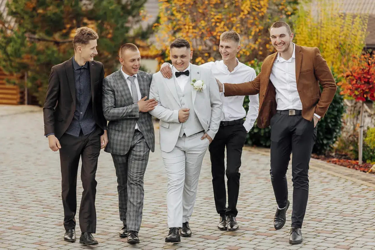 Pięciu mężczyzn w garniturach, w tym pan młody w jasnym stroju. Zastanawiasz się, jakich kolor&oacute;w nie ubierać na wesele?