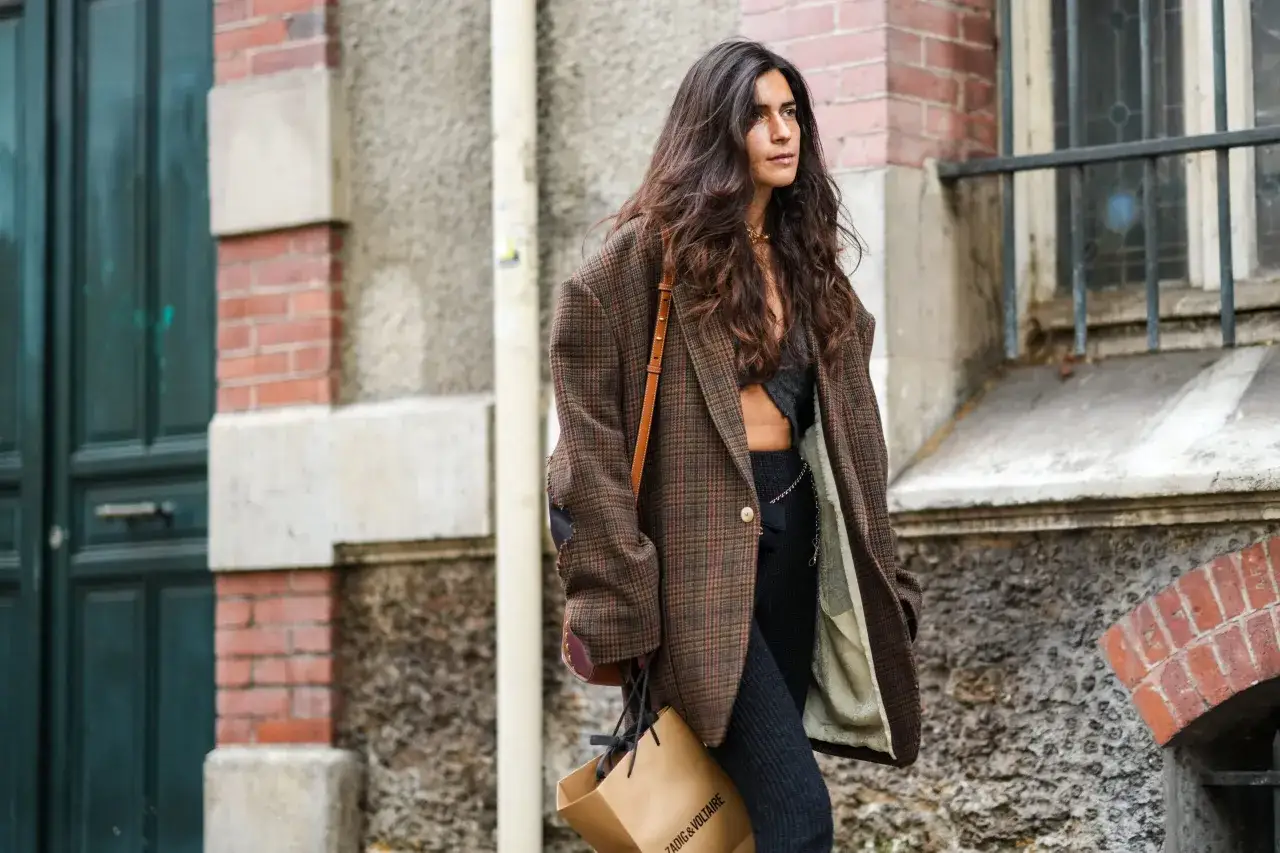 Kobieta w brązowej marynarce w kratę, tworzącej stylową stylizację. Torba z logo Zadig & Voltaire.