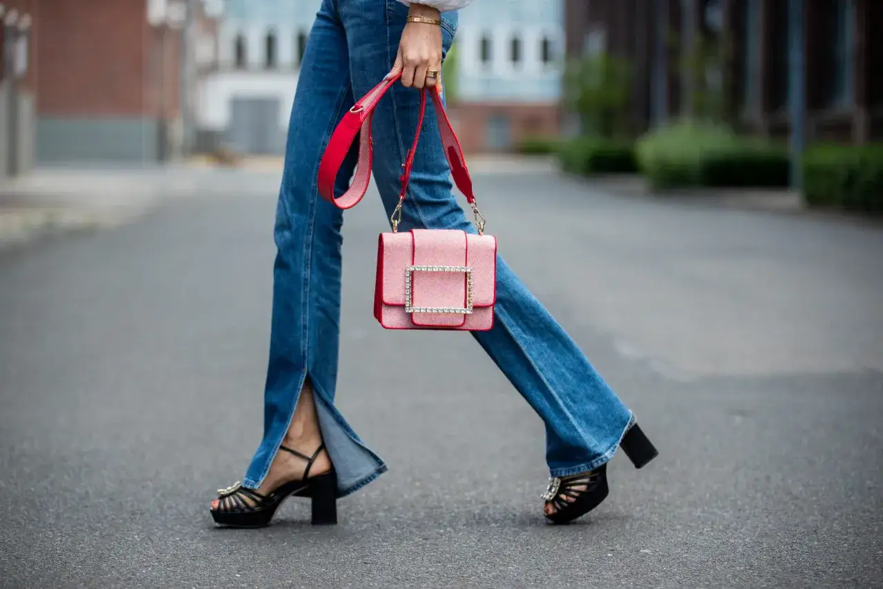 Stylowe jeansy bootcut z rozcięciami, czarne platformy i różowa torebka tworzą modny look.