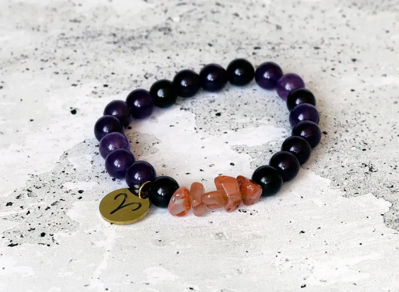 Bransoletka z kamieni dla barana, z symbolem zodiaku i koralikami w odcieniach fioletu i czerni.