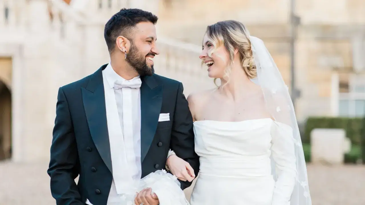 Para młoda w stylizacjach zgodnych z dress codem white tie: pan młody w czarnym fraku z białym poszetką i muszką, panna młoda w sukni ślubnej.